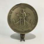 Antiga placa em metal cinzelado circular da " Escuela De Grumetes Alejandro Navarete C. Base no formato de rabo de peixe. Dimensões:16 cm X 13 cm  X 7 cm .