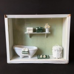 Miniatura de Toalet  com banheira, cesto de roupas e prateleira. Set emoldurado com vidro de proteção. Moldura precisando de restauro. Dimensões: 21 cm x 27 cm.