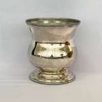 Vaso floreira em metal espessurado a prata decorado na borda e base com minusculos simbolos geométricos. Med. 18,5cm de altura X 17cm de diâmetro. Falta alças