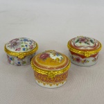 Lote com 3 (três) porta-pílulas em porcelana com metal dourado, decorados com flores, med. 4,5cm de diâmetro. 