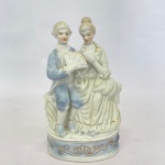 Estatueta em porcelana na cor branca com frisos dourados representando casal em cena româtica, med. 19cm de altura