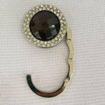 Suporte para bolsa em metal com pedra na cor ambar no centro e cristais brancos menores na borda, med. 4,5cm 
