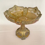 Fruteira/Centro de Mesa em metal espessurado a prata, com base e pés vazados decorado com coroas de flores. Med. 32cm de diâmetro e 30cm altura – Apresenta desgastes e base com parafuso solto.  