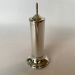 Paliteiro em metal espessurado a prata com pegador pontudo. Med.: 15,5cm de altura e 6cm de diâmetro.