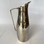 WOLFF - Jarra de suco em metal espessurado a prata, lisa, com alça reta. Med.: 25cm de altura e 12cm de largura. Apresenta pequena mossa na base