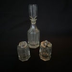 Combinado com galheteiro, saleiro e pimenteiro de vidro com base oitavada. Med.: 18cm de altura e 6cm de diâmetro o galheteiro, e apresenta rachadura no bocal. Pimenteiro com tampa quebrada.