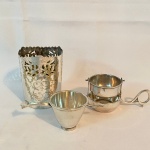 Lote com 3 (três) peças em metal espessurado a prata, sendo: Um coador para chá, um suporte para copo e um dosador. Apresenta desgaste