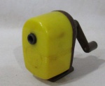 COLECIONISMO - Antigo apontador de lápis, da marca APSCO STAR HOME, confeccionado em pasticho rígido na cor amarela e ferro. Medida: 9 cm de altura. Com sinais de oxidação.