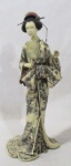 ESCULTURAS - Belíssima escultura oriental, confeccionada em resina, ricamente detalhada e policromada, representando "Gueixa". Medidas: 38,5 cm de altura x 15 cm de comprimento da base x 11,5 cm de largura da base..