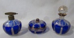 CRISTAIS - Dois perfumeiros e um porta joias em cristal veneziano translúcido e azul, trabalhado com figuras geometrizadas, arrematados com pintura feita à ouro, tampa e pega da tampa facetadas, sendo um guarnecido com metal dourado. Med. maior: 14,5 cm de altura total/ menor: 7 cm de altura total. Um perfumeiro e porta joias possui bicados nas bordas e na tampa.