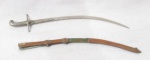 MILITARIA - Uma miniatura de espada com bainha, confeccionadas em metal, bainha com primorosa ornamentação cinzelada de elementos vegetalistas, medindo: 20,5 cm de  comprimento total .Com sinais de oxidação e bainha com rupturas.