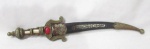 CUTELARIA / FACAS - Uma adaga confeccionada em metal, com primorosa ornamentação cinzelada em alto e baixo relevo, apliques em plástico rígido multicoloridos, com bainha em couro, medindo: 26 cm de  comprimento total. Possui sinais de oxidação.