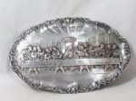 ARTE SACRA - Uma placa de parede em metal espessurado a prata, apresenta formato oval, com rico cinzelado em alto relevo representando "SANTA CEIA", bordas trabalhadas com volutas, flores e concheados. Medidas: 45 cm de comprimento x 30 cm de largura.