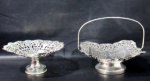 METAL PRATEADO - PRATA REGIA - DOMUS - Duas fruteiras em metal espessurado a prata, ornamentadas com delicado cinzelado, em formatos distintos, sendo uma redonda e uma em feitio de cesta, apoiadas sobre pé bolacha, com bordas recortadas e adornadas com decorações vazadas, marcadas na parte posterior das bordas. Medidas: maior: alt total (com a alça) 20 cm x larg 22,5 cm/ menor: alt 9,5 cm x diam 22 cm.