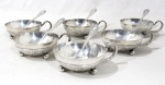 METAL PRATEADO - AEC 90 - Conjunto para sobremesa em metal espessurado a prata, composto por seis taças com primorosa ornamentação cinzelada relevada de motivos vegetalistas e cestos de frutos ao fundo, base tripoide com pés bolas, alça lateral curva. Acompanha seis colheres da manufatura EBERLE 90, com cabos decorados com folhas, volutas e arabescos. Marcados nas alças das taças e na parte posterior dos cabos das colheres. Medidas: taças: alt 3,8 cm x diam 9,2 cm/ colheres: comp 14,8 cm. Com discretas marcas de uso.