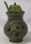 FAIANÇA - Um pote para mel em faiança vitrificada na cor verde, decorado com folhas e frutos em alto relevo, acompanha uma concha, medindo: alt total 18 cm x diam da borda 8,5 cm. Possui ínfimos bicados.