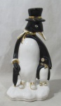 ESCULTURA - Grupo escultório em faiança vitrificada nas tonalidades branca e preta, representando "pinguim de cartola com seu filhote e guarda chuva", arrematado com exuberante pintura à ouro. Medidas: alt 29,5 cm x larg da base 12,5 cm. No estado, conforme fotos.
