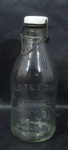 VIDRO - Antiga garrafa de Leite Vigor em vidro translúcido, capacidade para 1 litro, tampa em porcelana e metal, medindo: 24,5 cm altura. Com marcas do tempo.
