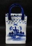 PORCELANA - DELFT BLUE/ HOLANDA - Uma cesta decorativa em porcelana vitrificada nas tonalidades branca e azul cobalto, pintada á mão, ornamentada com cenários de moinhos holandeses e elementos vegetalistas, bordas com decorações vazadas, marcada no fundo, medindo: 14,8 cm de altura x 8 cm de comprimento x 5 cm de largura.