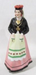 PORCELANA VISTA ALEGRE - Graciosa garrafa em porcelana vitrificada e ricamente policromada em forma de Dama com trajes típicos português, tampa em forma de chapéu, marcada no fundo. Medida: 27,5 cm de altura.