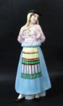 PORCELANA VISTA ALEGRE - Graciosa garrafa em porcelana vitrificada e ricamente policromada em forma de Dama com trajes típicos português, tampa em forma de chapéu, marcada no fundo. Medida: 27 cm de altura.