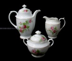 PORCELANA REAL S. PAULO- Um bule para café, uma cremeira e um açucareiro em porcelana nacional vitrificada branca, delicadamente decorados com flores e folhas em policromia, alças vazadas finalizando em volutas, pegas das tampas em forma estilizada de flor, arrematados com frisos à ouro, marcados no fundo. Medidas: maior (bule): alt total 16,5 cm x larg total 16 cm/ menor (açucareiro): alt total 10,5 cm x larg total 12 cm. Açucareiro com um bicado na parte interna da borda.