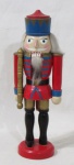 ESCULTURAS - Boneco Soldado da Guarda Real, clássico quebra-nozes, confeccionado em madeira com pátina em exuberante policromia, apoiado sobre base circular. Medidas: 24 cm de altura x 6,5 cm de diâmetro da base.
