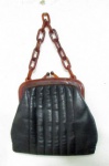 ACESSÓRIOS FEMININOS - Antiga bolsa feminina confeccionada em couro preto, encimada com fecho e uma alça anelada em plástico rígido (ou material similar) na cor caramelo, marcada IRMÃOS MASON na parte interna do fecho, medindo: alt total 36 cm x comp 23 cm. No estado.