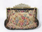 ACESSÓRIOS FEMININOS - Antiga bolsa feminina francesa em tecido gobelin com rico trabalho de motivos florais policromada, parte interna forrada em cetim com dois bolsos um porta níquel fixado por cordão, encimada com fecho, uma alça em corrente e aplique de flores e folhas vazadas em metal dourado. Medida: 25 cm de altura total x 19,5 cm de comprimento.