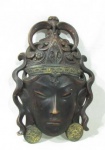 ECULTURAS - Escultura em madeira nobre, ricamente entalhada e patinada com toques de folhas de ouro velho, representando Rosto de Divindade Hinduísta. Med. alt 28,5 cm x larg da base 18,5 cm.
