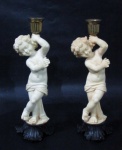 CANDELABRO / CASTIÇAL - Dois graciosos castiçais para uma vela, confeccionados em resina, com bobeche em metal dourado, seguido de coluna com escultura barroca italiana representando Putino, sobre base finalizando com folhas de acanto negras, medindo: alt 21 cm x larg da base 6,5 cm. Um com ínfimo bicado e com bicado no dedo mínimo. Vide foto extra!