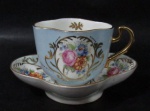 PORCELANA - LIMOGES - Uma xícara com seu respectivos pires, de coleção, em porcelana francesa vitrificada nas tonalidades branca e azul bebê, moldada em feitio diferenciado, decorada com motivos vegetalistas e arabescos em rica policromia e dourado, bordas generosamente filetadas à ouro, alça vazada com vasta douração, marcados no fundo. Medidas: xícara: alt 6,5 cm x comp 8,5 cm x larg 6,5 cm/ pires: comp 13,8 cm x larg 11 cm.