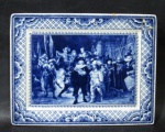 PORCELANA - DELFT - Antiga placa decorativa de parede, em fina porcelana vitrificada "Blue White", no padrão da renomada manufatura Holandesa Deflt, pintada á mão, apresentando cena intitulada "Nachtwacht" ("Vigília Noturna") Noor Rembrandt Night Watchman ao centro, seguido de bordas ligeiramente repuxadas e adornadas com motivos vegetalistas e geométricos, marcada na parte posterior, medindo: 17 cm de altura x 22 cm de largura. Possui colado na borda. Vide fotos extras!