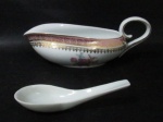 PORCELANA SCHMIDT - Uma molheira em porcelana vitrificada branca, decorada com motivos florais em rica policromia ao centro, seguido de bordas adornadas com guirlandas de folhas e arabescos, generosos filetes e gregas em pintura à ouro, sobre faixa esmaltada na tonalidade rosa, alça vazada arrematada com frisos em douração, marcada no fundo. Med. molheira: alt 6,5 cm x larg total 23,5 cm/ colher: 13,3 cm. Acompanha uma colher da mesma porcelana. Em ótimo estado!