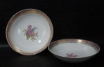 PORCELANA SCHMIDT - Duas tigelas em porcelana vitrificada branca, com tamanhos distintos, decoradas com motivos florais em rica policromia ao centro, seguido de bordas adornadas com guirlandas de folhas e arabescos, generosos filetes e gregas em vasta pintura à ouro, sobre faixa esmaltada na tonalidade rosa, marcadas no fundo. Med. maior: alt 6 cm x diam 24 cm/ menor: alt 5,5 cm x diam 22 cm. Tigela maior com bicado na borda, conforme foto extra.
