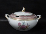 PORCELANA SCHMIDT - Uma sopeira em porcelana vitrificada branca, decorada com motivos florais em rica policromia ao centro, seguido de bordas adornadas com guirlandas de folhas e arabescos, generosos filetes e gregas em pintura à ouro, sobre faixa esmaltada na tonalidade rosa, pega da tampa em forma estilizada,  alças finalizando em folhas e arrematadas com vasta douração, marcada no fundo. Med. alt total 16 cm x larg total 29 cm. Em ótimo estado!
