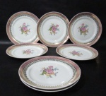 PORCELANA SCHMIDT - Sete pratos para sobremesa em porcelana vitrificada branca, decorados com motivos florais em rica policromia ao centro, seguido de bordas adornadas com guirlandas de folhas e arabescos, generosos filetes e gregas em pintura à ouro, sobre faixa esmaltada na tonalidade rosa, marcados no fundo. Med. 18,2 cm de diâmetro. Um com ínfimo bicado na borda.