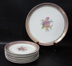 PORCELANA SCHMIDT - Um prato para bolo com sete pratinhos, em porcelana vitrificada branca, decorados com motivos florais em rica policromia ao centro, seguido de bordas adornadas com guirlandas de folhas e arabescos, generosos filetes e gregas em pintura à ouro, sobre faixa esmaltada na tonalidade rosa. Med. maior: 28,5 cm de diâmetro/ menor: 18,2 cm de diâmetro.