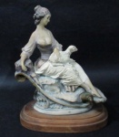 ESCULTURAS - Belíssima escultura em resina italiana, ricamente detalhada e policromada, representando "Dama sentada em pedra com carneiro no colo", sobre base de madeira em formato oval, assinatura não identificada. Medidas alt 21 cm x comp da base 16,5 cm x larg da base 12 cm.