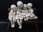 ESCULTURAS - Gracioso grupo escultórico em estuque, ricamente detalhado, representando "Menino e Meninas sentados em banco de madeira lendo livro", marcado com etiqueta do fabricante no fundo. Medidas totais: alt 26 cm x comp da base 28 cm x larg da base 8 cm. Possui um bicado no pé, e banco com falhas na madeira. Vide fotos extras!