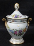 PORCELANA - EL GRECO - Elegante açucareiro em fina porcelana vitrificada branca, ornamentado com guirlandas de flores e folhas em rica policromia, pega da tampa em forma estilizada de pinha, alças laterais finalizando em volutas, guarnecido com vasta pintura à ouro nas bordas, nas pegas e na base, apoiado sobre pé bolacha, marcado no fundo. Med. alt total 19,5 cm x diam da borda 11 cm.