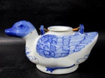 PORCELANA MADE IN CHINA - Chaleira em porcelana oriental vitrificada nas tonalidades branca e azul, pintada à mão, moldada em formato de pato, com alça articulada em rattan, marcada no fundo. Med. alt 11,5 cm x comp 21,5 cm, aproximadamente.