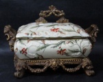 PORCELANA - Diferenciada e antiga caixa porta joias, confeccionada em porcelana policromada, com rica ornamentação de elementos vegetalistas, com pega da tampa, alças laterais e base em resina esmaltada com folhas de ouro velho ricamente trabalhada com guirlandas de flores e folhas de acanto, base quadrupede com pés em curvos. Medidas: alt total 18 cm x larg total 27,5 cm.