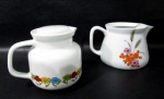 PORCELANA - POZZANI / REAL S. PAULO - Duas leiteiras em porcelana vitrificada branca decoradas com flores e folhas de trigo em rica policromias, tendo uma a tampa em plástico resistente, e uma sendo refratária para chama direta, alças vazadas, marcadas no fundo. Med. alt total 13,5 cm x larg total 15,5 cm/ menor: alt 12 cm x larg total 20 cm.