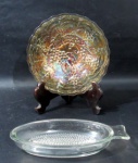 VIDRO - Duas antigas peças sem vidro, sendo: A) um prato para compoteira em vidro Carnival Glass dito fogo, ricamente trabalhado, com decoração de cachos de uva e folhas de parreira em relevo, bordas com movimento ondular, medindo: 16 cm de diâmetro; B) um ralador de frutas em vidro translúcido, moldado em formato de peixe, medindo: 18,5 cm de comprimento x 9,5 cm de largura.