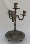 METAL PRATEADO, um (1) candelabro para quatro lumes, fuste de hastes cilíndricas e sobrepostas, terminando em bobeche, do último cilindro saem três braços em torçaide, também terminando em bobeche, assente sobre prato com borda drapeada e cinzelada em ondulados, tracejados e perolados, base relevada, trípode com terminações em garra, volutas e elementos vegetalistas, puncionado MEXICANA, medindo 31,5 cm altura.