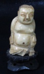 ESCULTURAS - Escultura em bloco de marfim retratando Buda, apoiado sobre peanha em madeira. Medidas totais: altura: 7 cm x largura da base: 3,5 cm.