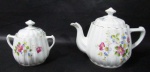 PORCELANA - SCHMIDT - Belíssimos bule e açucareiro em porcelana nacional vitrificada branca, moldados em canelados, ornamentados com motivos vegetalistas em exuberante policromia, alças vazadas trabalhadas com volutas relevadas, pegas das tampas em forma estilizada de flor, bordas filetadas à ouro, marcados no fundo. Med. bule: alt total 16 cm x larg total 23 cm/ açucareiro: alt total 12 cm x larg total 13,5 cm.