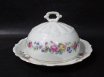 PORCELANA C. T. MADE IN POLAND - Elegante manteigueira em porcelana polonesa vitrificada branca, ornamentada com motivos vegetalistas em exuberante policromia, bordas recortadas com movimento ondular e filetadas à ouro, pega da tampa em forma estilizada de laço, marcada no fundo. Medidas: alt total 9,5 cm x  diam total 18 cm.
