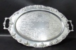 METAL - Grande bandeja ovalada em metal espessurado a prata, fundo cinzelado em arabescos, bordas e alças realçadas com uvas e folhas de parreira. Medidas comp 66 cm x larg 41,5 cm.